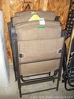 Four chairs folded and stacked showing padded tan covers and black frames