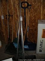Photo showing snow shovels (blue plastic blades) and leaf rakes against plywood wall