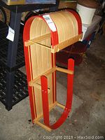 Side view of child's wooden sleigh showing arched backrest and red trim runners