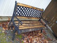 Front angled view of outdoor bench showing cast metal frame and worn wood slats seat and backrest with lattice metal design.