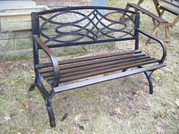 Front view of outdoor metal park bench with wooden slat seat and ornamental scrollwork on backrest.