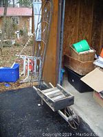 Photo showing wooden wheelbarrow with metal wheel and two metal trellis panels leaning against a wooden door in an outdoor setting.