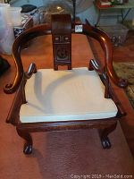 Front view of the Asian inspired vintage wooden armchair with a white cushioned seat showing carved patterns on the backrest and claw foot legs.