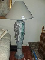 Full view of the floor lamp showing the entire piece including the beige lampshade and the elephant and leaf motif base.