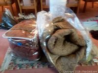 Photo of two king size comforters, one in plastic bag and one rolled up, placed on the decorative area rug.