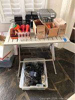 Wide view of both coin sorters on folding table with accessories on surface and a plastic bin of adapters underneath