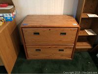 Front view of two drawer wooden filing cabinet showing wood grain finish and inset metal handles.