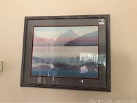 Framed wall art print showing mountain and lake landscape hanging on wall with visible reflections.