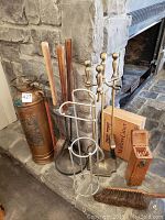 Fire extinguisher, fireplace tool sets, match holder, wooden box, and broom arranged on stone hearth.