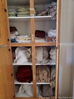 Closet shelves filled with various folded and loosely stacked sheets and towels in beige, brown, white, maroon, and light green colors.