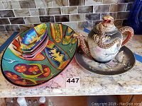 Full view of teapot with dragon motif, matching plate, large colorful plate and five smaller colorful plates stacked.