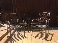 Four metal patio chairs with ornate lattice backs and slatted seats arranged outdoors on a deck showing natural lighting and shadows.