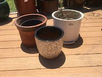 Two outdoor pots on wooden decking: one large rustic clay pot and one smaller speckled ceramic pot.