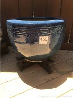 Large blue ceramic pot with geometric band and wood pedestal on wooden floor.