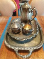 Photo showing full tea set and two trays on a wooden table with chairs in the background.