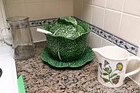 View of three items on granite countertop including the clear etched glass jug, cabbage soup tureen with ladle and matching plate, and the Botanic Garden ceramic jug with flower design.