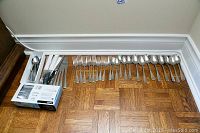 Wide photo showing all stainless steel flatware arranged on floor including spoons, forks, knives, plus box of new plastic cutlery on left.
