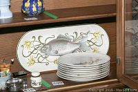 Fish serving platter and stack of eight fish plates in wooden cabinet shelf.