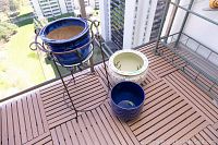 Overview of three ceramic cache pots grouped with metal plant stand on balcony wooden floor with buildings in background.