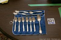 Overview of all spoons and olive pick on blue felt roll-up pouch on table