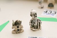 Two carved netsuke figurines displayed side by side on a flat surface. One figurine shows a seated man with a traditional hairstyle and robe, and the other a kneeling figure with a detailed mask and drum object.