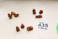 Photo showing nine carved animal netsuke, arranged on a white background, showcasing variety including birds, dogs, and other small animals.