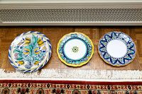 Three hand painted Italian pottery plates arranged in a row on the floor showing each plate's unique design