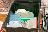 Black plastic bin with various plasticware containers and lids inside, stacked neatly.