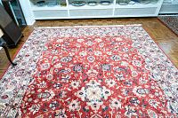Full view of red floral-pattern wool area rug on parquet floor under display shelves