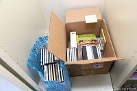 Box containing approximately 30 classical music CDs and boxed sets along with a blue patterned shopping bag filled with additional CDs.