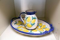 Full view of the artisan pottery set showing the platter with lemon design and the pitcher placed inside it.