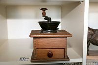 Front view of the antique wooden coffee grinder with visible hand crank, metal bowl, and wooden drawer.