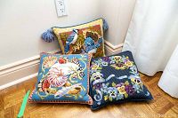 Three colorful needlepoint cushions arranged on a hardwood floor, showing all cushions with different themes.