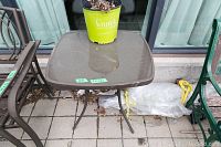 Square outdoor table with glass top and metal base, shown from above with a plant pot on top.