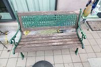 Full image of outdoor bench showing metal frame with green paint and wooden slats seat showing heavy wear