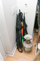 Photo showing six umbrellas standing in corner against wall with ceramic decorative vase beside them.
