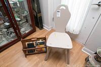 Shows painted chair and wooden magazine rack side by side in room near door.