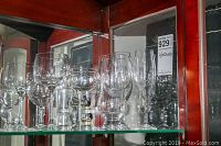 Assorted twelve pieces of glassware displayed on glass shelf, variety of sizes and shapes including shot glasses and drinking glasses