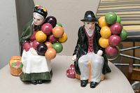 Pair of faux porcelain figurines depicting elderly man and woman each holding colorful ball bouquets, sitting on a flat surface.