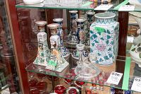 Display cabinet showing porcelain candle holders, large floral vase, glass candle holder, and part of horse jumping artwork.