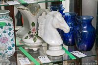 Front angle of white horse head sculpture and decorative vase on glass shelf with blue vases in background