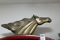 Brass horse head sculpture shown from side angle on a wooden surface with auction tag.