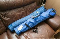 Two blue carry bags containing folding armchairs, placed on a brown leather sofa.