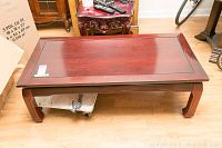Full view of the wooden coffee table showing the rectangular paneled top and curved legs, with some scuffs and wear visible