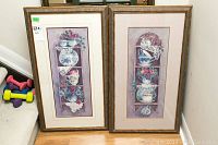 Two framed prints side by side on floor showing floral teacups and vases artwork with pastel tones and gold frames