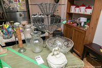 Wide view of lot on table showing wire two-tier fruit server, glass bowl, angel container, candle holders, and other decorative pieces.