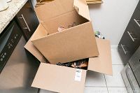 Two open cardboard boxes filled with multiple wooden clothing hangers placed in a kitchen setting.