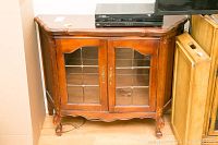 Front view of wood cabinet showing glass doors with metal grid design and brass handles. Cabinet legs have intricate carvings.