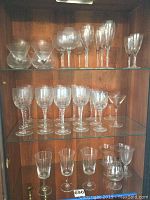 Various Towle crystal stemware glasses on shelves in wooden cabinet, assorted types, incomplete sets