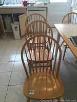 Six oak dining chairs arranged in kitchen, showing natural wood finish and spindled backs.